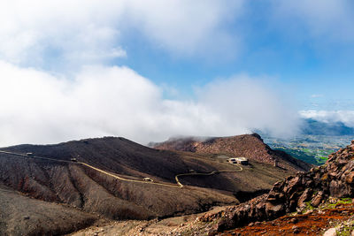Panoramic view of volcanic landscape, abandoned cable car, and aso town against sky