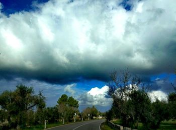 Road by trees against storm clouds