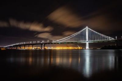 Illuminated bridge over river against sky at night