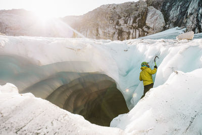 Side view of man ice climbing outside of glacial cave.