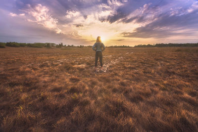 Rear view of man standing on land against sky during sunset