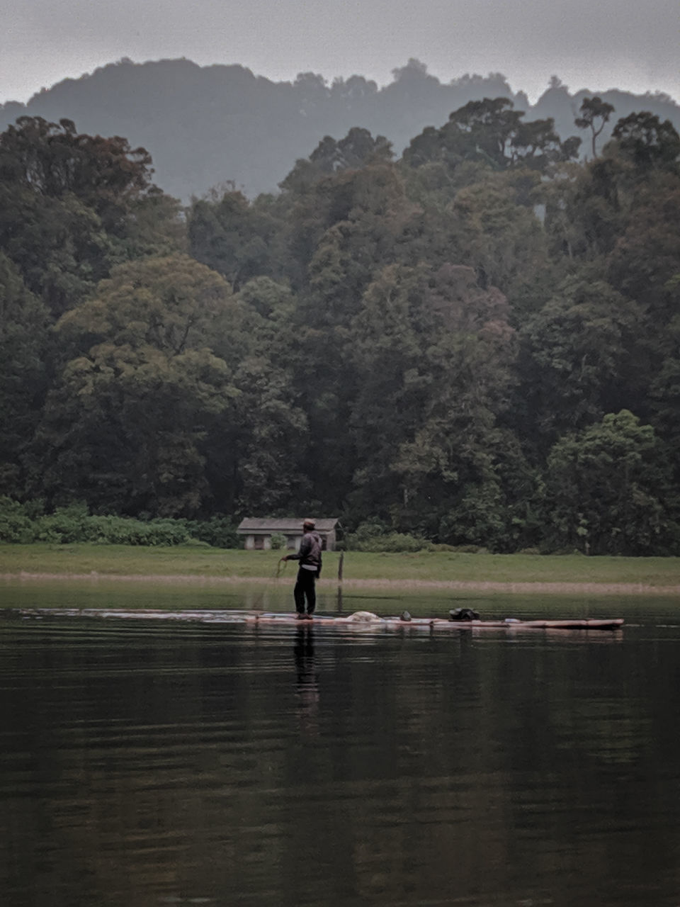 MAN STANDING ON MOUNTAIN BY LAKE AGAINST MOUNTAINS