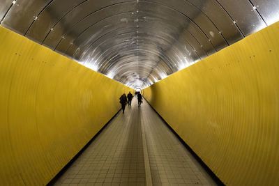 Rear view of people walking in illuminated tunnel