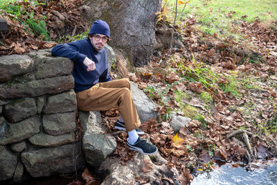 Young man sits against a stone wall in outdoor autumn background