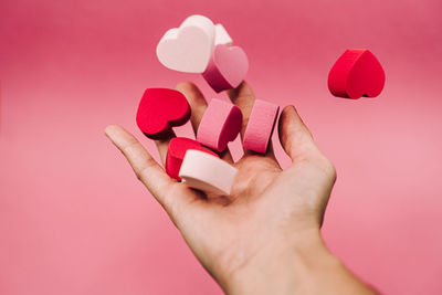 Close-up of hand holding heart shape against pink background
