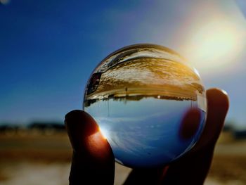 Cropped hand holding crystal ball against sky