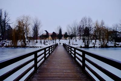 Footbridge over frozen lake against sky