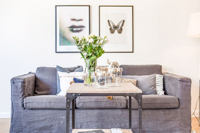 Plants in vase on table by sofa against paintings hanging on wall at home