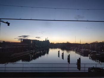 Reflection of silhouette electricity pylon in city against sky during sunset