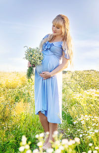 Pregnant woman with flowers while standing on field