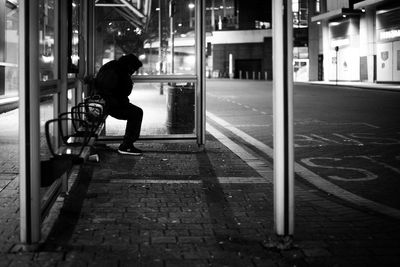 Side view of man sitting on bus sop in city at night