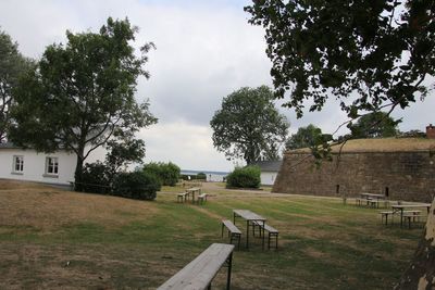 Park bench on field by building against sky