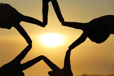 Close-up of silhouette hands making star shape against sky during sunset