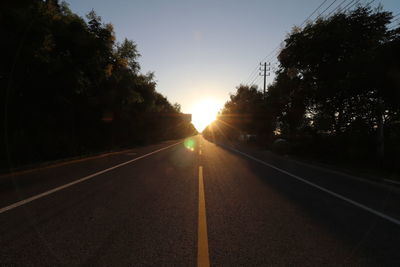 Road amidst trees against clear sky during sunset
