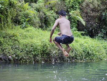 Full length of shirtless man jumping in forest