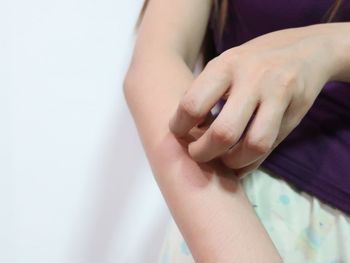 Midsection of woman scratching arm against white background