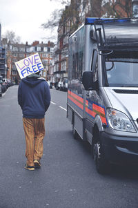 Rear view of a man walking with placard on road