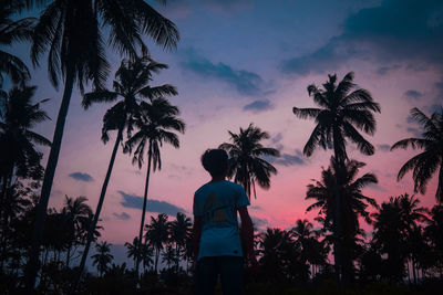 Silhouette man standing by palm trees against sky during sunset