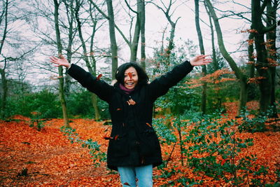 Portrait of woman with arms outstretched standing at forest during autumn