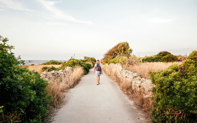 Rear view of person walking on road by sea against sky