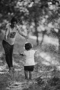 Mother and daughter playing amidst spraying water on land