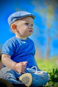 Portrait of a boy taken from below sitting against a blue sky wearing a blue beret and t-shirt blu