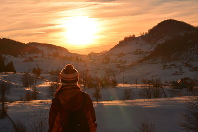 Rear view of hiker standing on snow covered mountain against sky during sunset