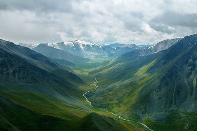 Green mountain gorge in summer with river, snow-capped peaks in the distance, sky with clouds