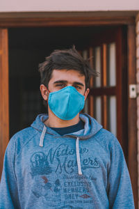 Portrait of young man wearing mask standing against house