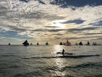 Silhouette people on sea against sky during sunset