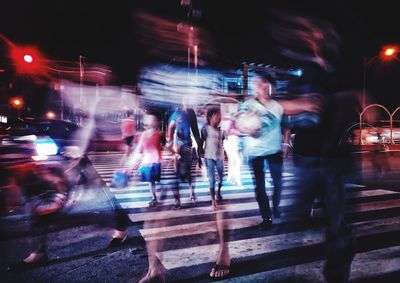 Blurred motion of people walking on illuminated street at night