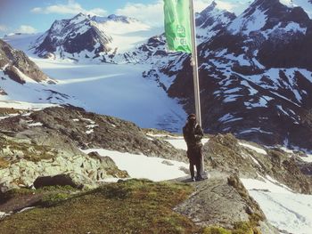 Person standing by green flag against snow covered mountains