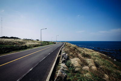 Road leading towards sea against blue sky