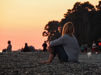 Rear view of couple sitting on land against sky during sunset