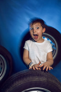 Boy in a white t shirt shirt and hat sits on a background of car wheels on a blue