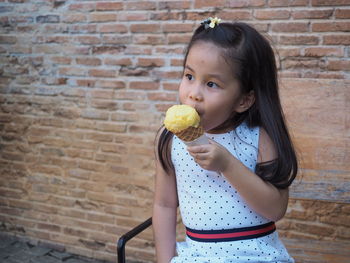 Cute girl holding ice cream against brick wall