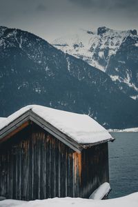 Snow covered hut at lake and mountain against sky