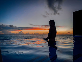 Silhouette of man standing by sea against sky during sunset