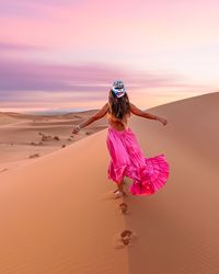 Girl in a pink sand on the top os the sand dunes in the sahara desert morocco, running leaving footp