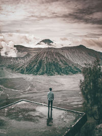 Rear view of man standing against mountain and cloudy sky