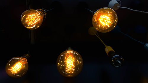 Low angle view of illuminated light bulbs against black background