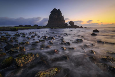 Rock formation on beach against sky during sunset