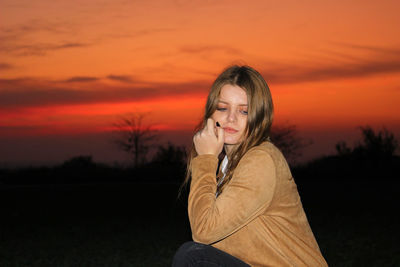 Young woman sitting on field against orange sky
