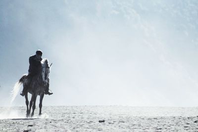 Man riding horse at beach against sky