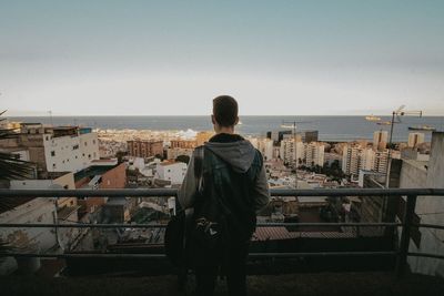 Rear view of man looking at cityscape against clear sky