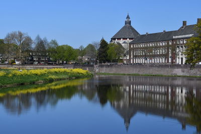 Reflection of building and trees in lake against clear blue sky