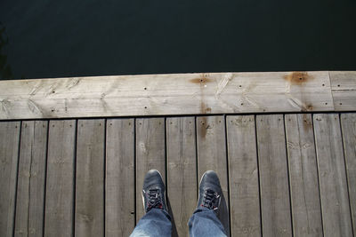 Low section of person standing on pier over lake