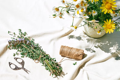 Yellow chamomile and bunch of fresh scented organic sage flowers on white linen tablecloth.