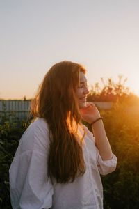 Beautiful young woman standing against sky during sunset