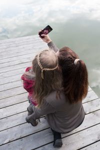 Mother taking selfie with daughter on pier over lake